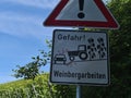 Metal road sign with red frame and exclamation mark warning of accidents that could be caused by works in the vineyards.