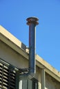 Metal rooftop chimney vent for fireplace or industrial purposes on side of building with blue copy space sky background Royalty Free Stock Photo