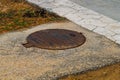 Metal rusty cover from the inspection hatch of sewer street communications on the sidewalk in the park near the stone fence