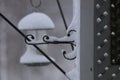 A metal, scrolled plant hanger attached to a wood trellis covered in snow during a snowstorm in Wisconsin