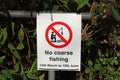 metal sign fixed to a metal post by the edge of a river, warning that course fishing is not allowed between March and June Royalty Free Stock Photo