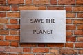 A metal sign with the words SAVE THE PLANET is affixed to a rustic brick wall. Sunlight casts shadows, emphasizing the urgent Royalty Free Stock Photo