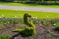 A metal snake covered with lush green leaves in the garden surrounded by colorful flowers and lush green grass and trees