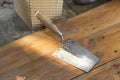 Metal spatula with wooden handle in dry gray plaster putty. Old tool laying on the wooden floor of home terrace.