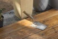 Metal spatula with wooden handle in dry gray plaster putty. Old tool laying on the wooden floor of home terrace.