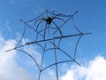 Metal spider in a web against the sky