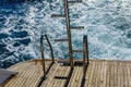 Metal staircase for descent into the water and wave trace with white foam on a water surface behind of fast moving yacht Royalty Free Stock Photo