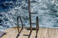 Metal staircase for descent into the water and wave trace with white foam on a water surface behind of fast moving yacht Royalty Free Stock Photo