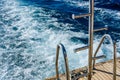 Metal staircase for descent into the water and wave trace with white foam on a water surface behind of fast moving yacht Royalty Free Stock Photo