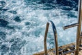 Metal staircase for descent into the water and wave trace with white foam on a water surface behind of fast moving yacht Royalty Free Stock Photo