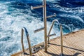 Metal staircase for descent into the water and wave trace with white foam on a water surface behind of fast moving yacht Royalty Free Stock Photo