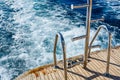 Metal staircase for descent into the water and wave trace with white foam on a water surface behind of fast moving yacht Royalty Free Stock Photo