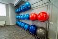 Metal stand at the wall with coloured fitness balls in the light gym. Yoga and pilates hall with sport equipment inside