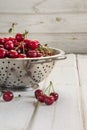 Metal strainer with ripe berries and cherry on wooden background. Colander filled with cherries over a rustic board.