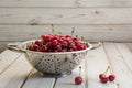 Metal strainer with ripe berries and cherry on wooden background. Colander filled with cherries over a rustic board.