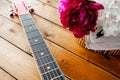 Metal strings on the neck of an acoustic guitar and a bunch of lush fresh colorful peonies in a wicker basket on wooden boards,