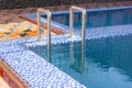 A metal swimming pool safe ladder (skimmer) on the entrance to the home inground poolside with the blue clean water.