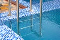 A metal swimming pool safe ladder (skimmer) on the entrance to the home inground poolside with the blue clean water