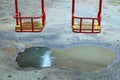 Metal swing with a wooden seat on a kids playground on a rainy day with a puddle under it