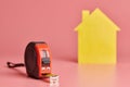 Metal tape measure funny concept. House renovation. Home repair and redecorated concept. Yellow house shaped figure on pink