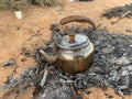 A metal teapot containing tea cooked over a wood fire in the desert Royalty Free Stock Photo