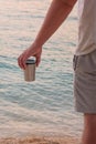 Metal thermo cup in hand on coastline. Enjoy a tasty drinks during trips. Sea background. Voyager