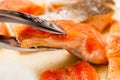 Metal tongs holding red trout fillet, also known as arctic char
