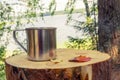 A metal tourist mug stands on a stump against the background of a large pond