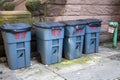 Metal trash cans side by side in an alley, each with a number painted on them.