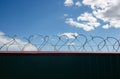 Metal wall with barbed wire against the blue sky background. Royalty Free Stock Photo