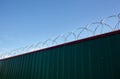 Metal wall with barbed wire against the blue sky background. Royalty Free Stock Photo