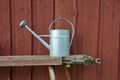 Metal watering can on bench besides red wooden wall Royalty Free Stock Photo