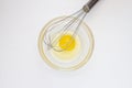 Metal whisk and chicken yolk in a glass bowl