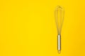 Metal whisk for whipping on a yellow background.