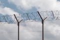 Metal wire fence with barbed wire on the background of blue sky, white clouds. Barbed wire fence close-up, border, protected area Royalty Free Stock Photo