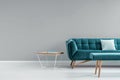 Metal and wood end table with book standing next to turquoise sofa with pillow in real photo of grey living room interior with pla Royalty Free Stock Photo