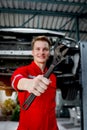 Metal wrench spanner in hand of mechanic in red uniform standing near lifted vehicle, auto mechanic check wheel at garage,