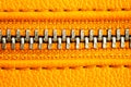 Metal zipper on intense orange leather jacket or purse detail close up macro. The zipper is tightly closed binding together.