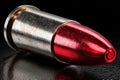 Metallic bullet with a red tip rests on a dark reflective surface, symbolizing danger and force Royalty Free Stock Photo
