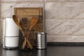 Metallic cups and kithcne utensils in it,white paper towels and wooden board on the black table against marble wall.Empty space