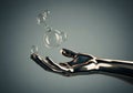 Metallic hand reaching out to catch floating bubbles in a serene setting