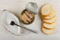 Metallic jar with canned pink salmon, plate and fork, pieces of bread on table. Top view