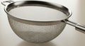 A metallic kitchen strainer with a fine mesh netting, featuring a circular frame and