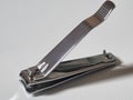 A close-up photo of a metallic nail clipper placed on a white surface with its lever raised, ready for use. Royalty Free Stock Photo