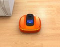 Metallic orange robotic vacuum cleaner moving on flooring