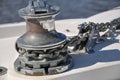 Metallic rusty anchor windlass on a white boat at the sea. Anchor is pulled up with the winch and chain. Metal looks shiny in the Royalty Free Stock Photo