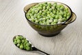 Spoon with green peas, brown bowl with frozen green peas on wooden table