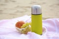 Metallic thermos with hot drink, fruits and plaid on sandy beach Royalty Free Stock Photo