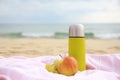 Metallic thermos with hot drink, fruits and plaid on sandy beach near sea Royalty Free Stock Photo