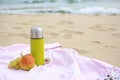 Metallic thermos with hot drink, fruits and plaid on sandy beach near sea, space for text Royalty Free Stock Photo